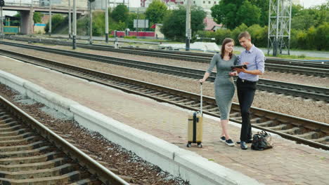 a man and a woman are standing on a railway platform in the countryside