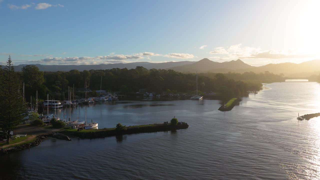 Aerial view of Brunswick Heads river at sunset, showcasing serene waters, boats, and lush surroundings with warm, golden lighting