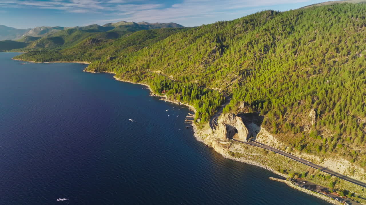 Delightful sight of stunning mountains overgrown with pine tree forest. Highway at the waterfront close to the water of Lake Tahoe, California, USA. Aerial view.