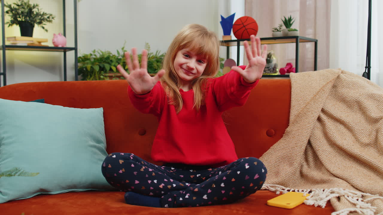 Child kid girl smiling friendly at camera waving hands gesturing hello hi greeting at home on couch