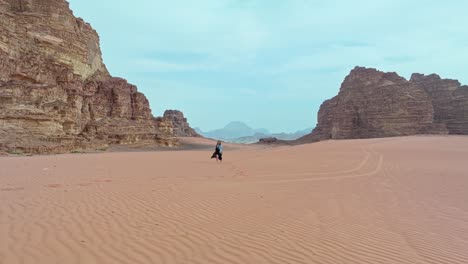 Scenic-Landscape-Of-Wadi-Rum-With-Woman-Walking-In-The-Desert-In-Jordan---aerial-drone