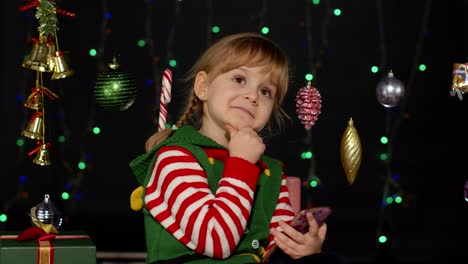 niña con disfraz de elfo de navidad haciendo compras en línea usando teléfono móvil, navegando en redes sociales