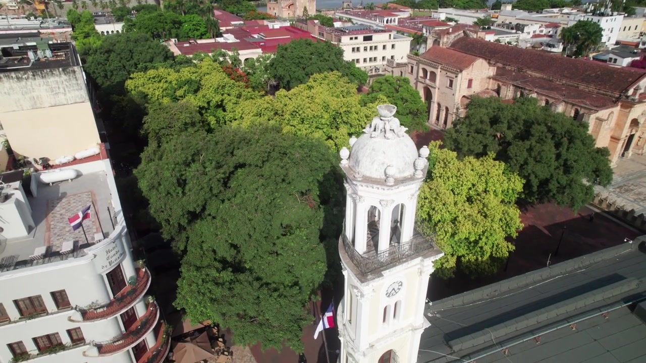 Ripresa a piedistallo con drone che scende oltre la storica torre dell'orologio bianca del Palacio Consistorial, rivelando una piazza urbana e architettura coloniale sotto un cielo blu