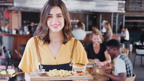 portrait of waitress serving food in busy bar restaurant smiling at camera