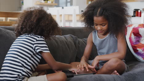 brother and sister sitting on sofa at home playing with digital tablet