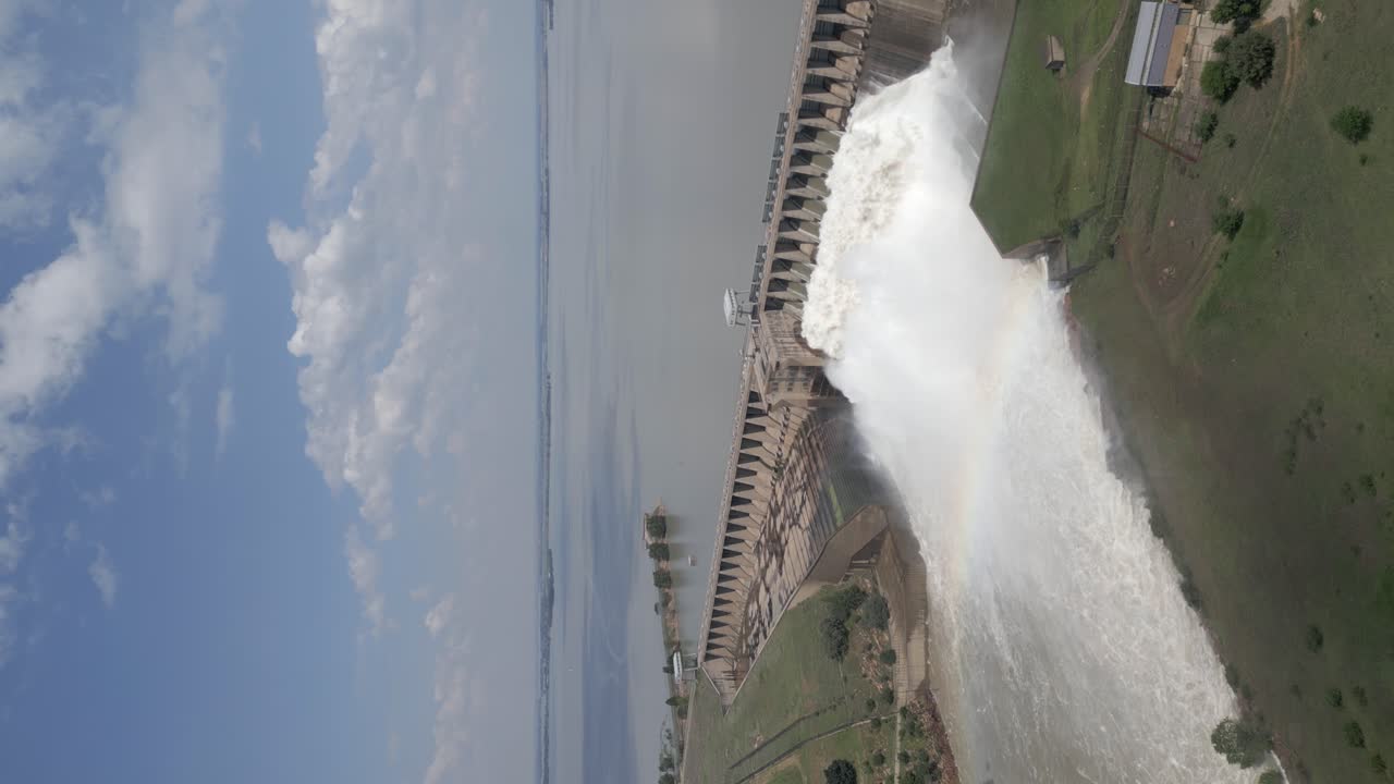 Vertical format: Hydroelectric dam releasing flood water forms rainbow