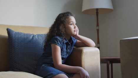 Mixed-race-thoughtful-girl,-sitting-on-soda-in-living-room