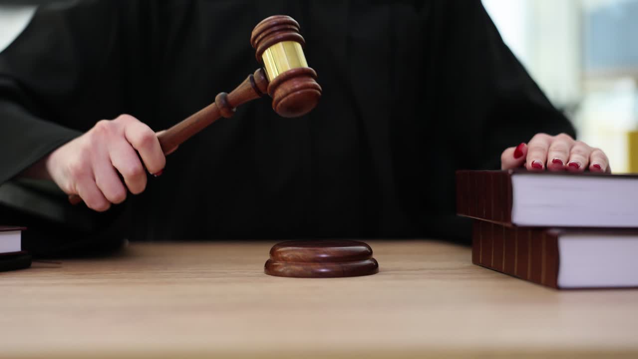 Giudice con toga batte il martelletto su un blocco sonoro, seduto al tavolo.