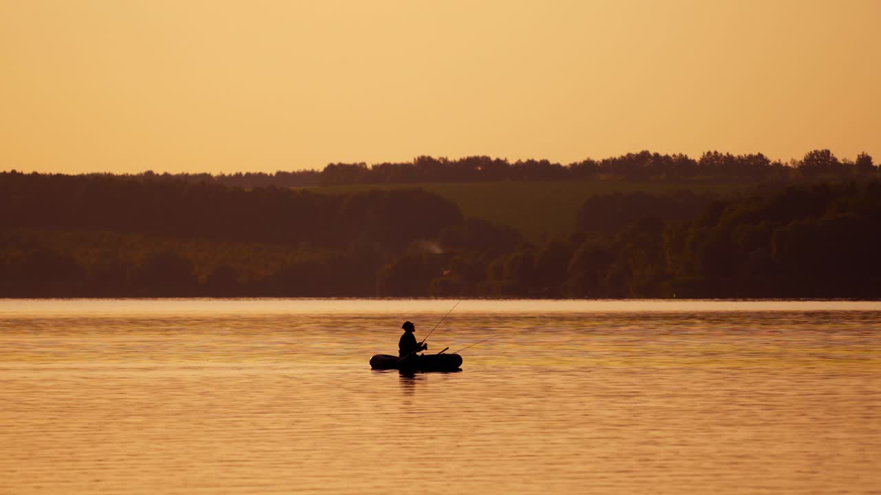 Fisherman in a boat silhouette. Mature man fishing from the boat on the pond at sunset