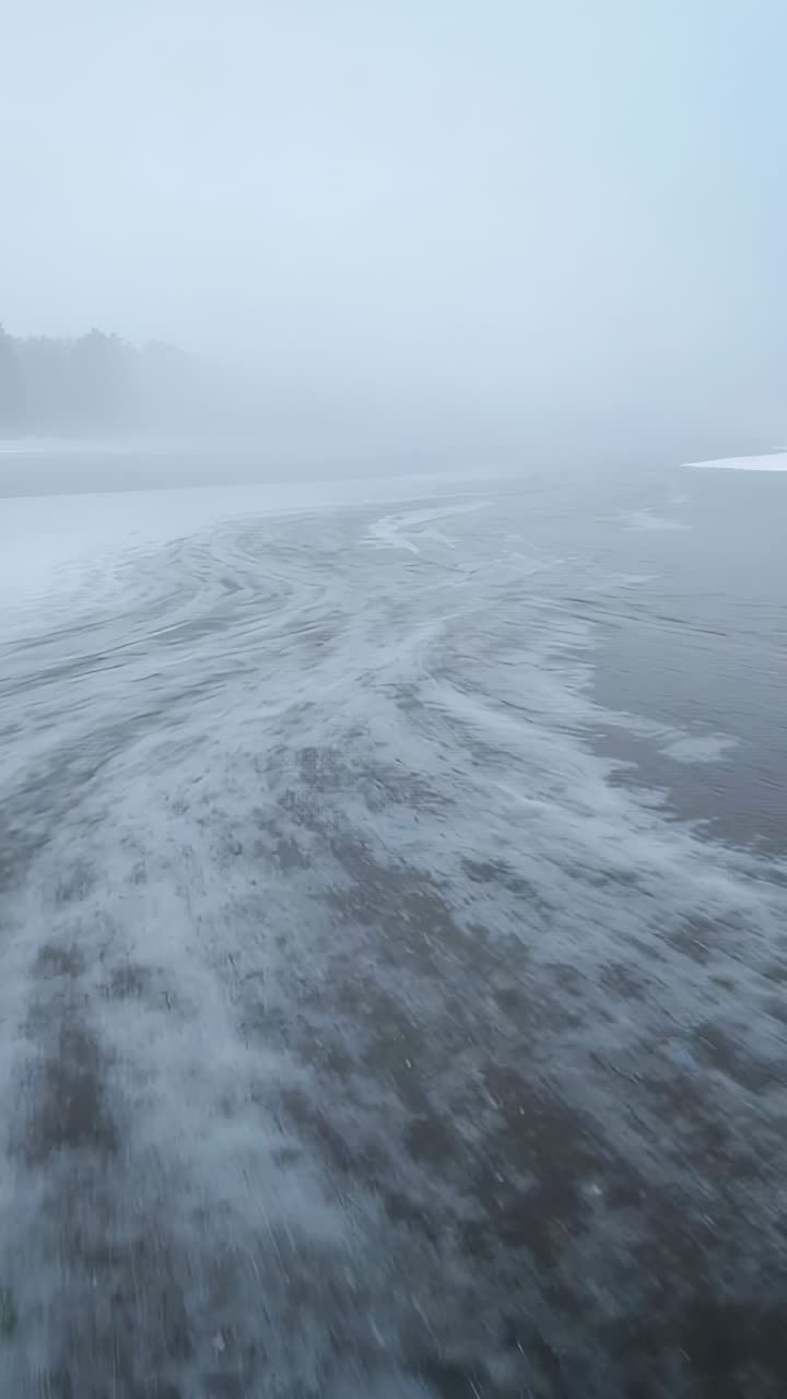 Vertical video: Moving cam revealing foam lines on ice shore, showing mist, left trees, right snow