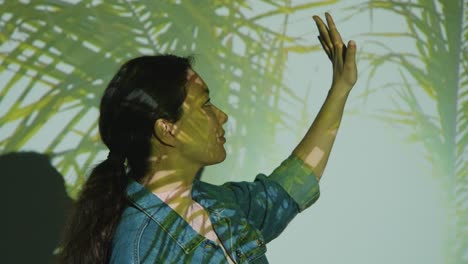 woman visiting immersive art exhibition with images of palm leaves being projected onto her face