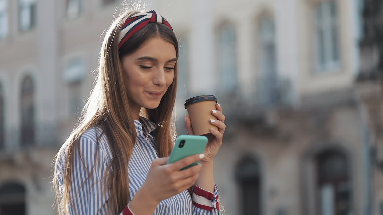 Giovane donna sorridente che beve caffè e usa lo smartphone in città