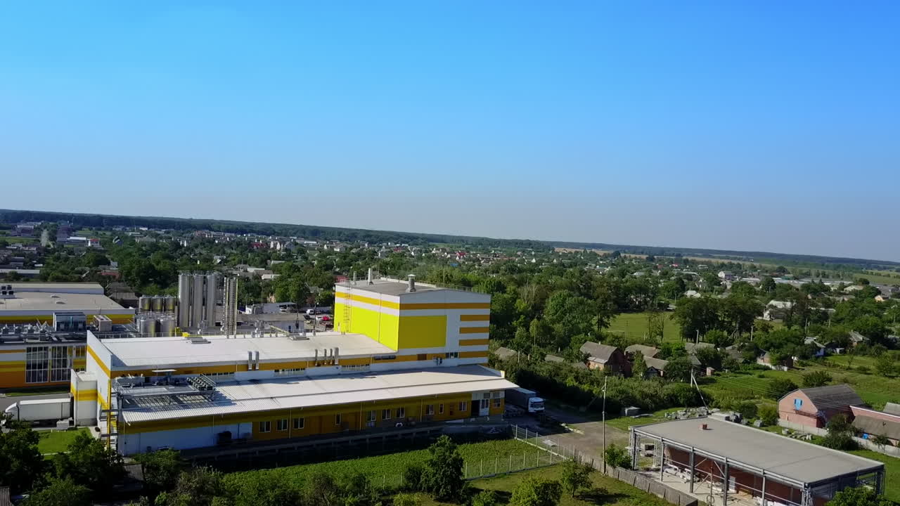 Big white and yellow building of an industrial plant located in the rural area. Aerial perspective. Blue clear sky at backdrop.