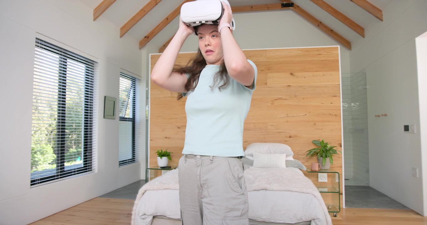 Donna che indossa un visore VR si muove su un tappeto a pelo lungo in camera da letto, testando il dispositivo e poi ispezionando il visore