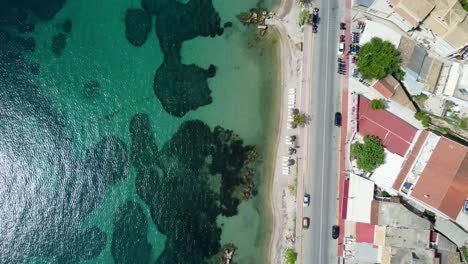 vista de drones de arriba hacia abajo de las aguas turquesas en la playa de ipsos, corfú, grecia, en contraste con los coches en la carretera costera
