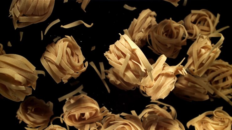 Rallentatore di tagliatelle secche che cadono su sfondo nero.