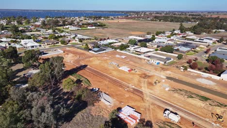 Vista-Aérea-En-Ascenso-De-Una-Nueva-Zona-De-Construcción-Residencial-Con-El-Lago-Mulwala-Más-Allá