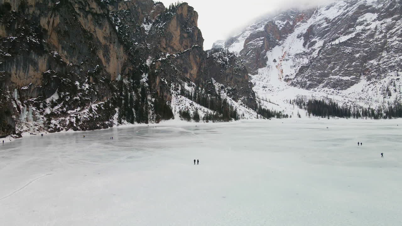drone volando sobre el lago congelado braies en trentino con gente caminando en el frío día de invierno