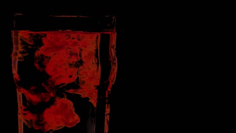 gotas rojas en un vaso de agua con fondo negro