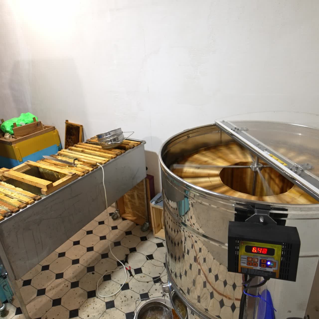 Little room with honey extractor machine, metal box of frames and a pile of wooden hives. Centrifuge working pumping honey. Top view