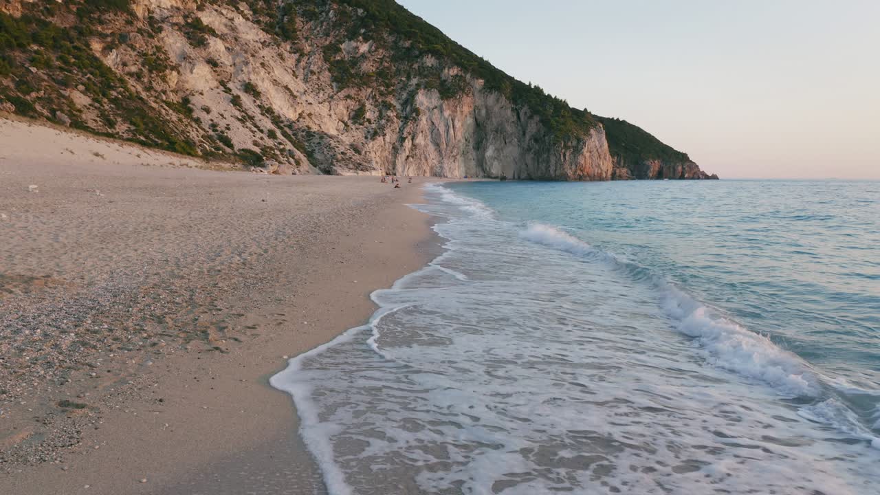Aerial low altitude view of beautiful Milos beach of Lefkada, Ionian island, Greece. Sunset golden sunlight and pristine waves breaking the turquoise blue sea on the shore