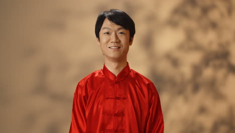 Cheerful-young-Asian-man-in-red-traditional-costume-smiling-at-camera