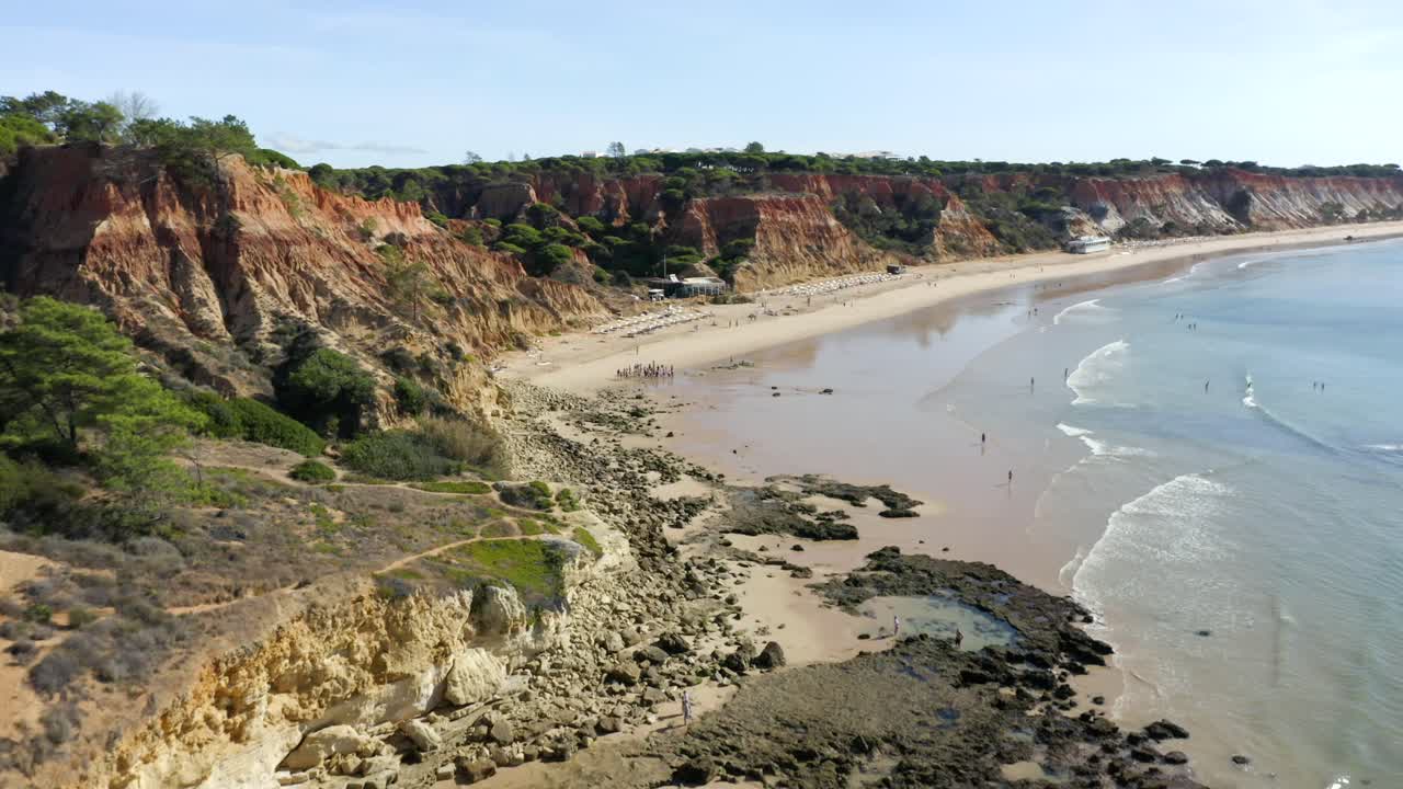 Turisti sulla spiaggia di Barranco das Belharucas con costa sabbiosa e onde calme in estate vicino ad Albufeira, Portogallo