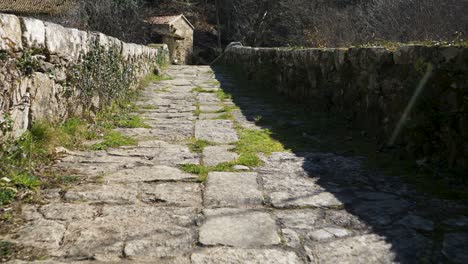 Spaziergang-Entlang-Der-Mittelalterlichen-Navea-Brücke-Mit-Sonneneinstrahlung,-Während-Gras-Zwischen-Den-Rissen-Wächst