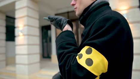 vista lateral de un ciego con gafas de sol con un brazalete amarillo con tres puntos negros mientras sostiene un teléfono inteligente y tiene una llamada con manos libres