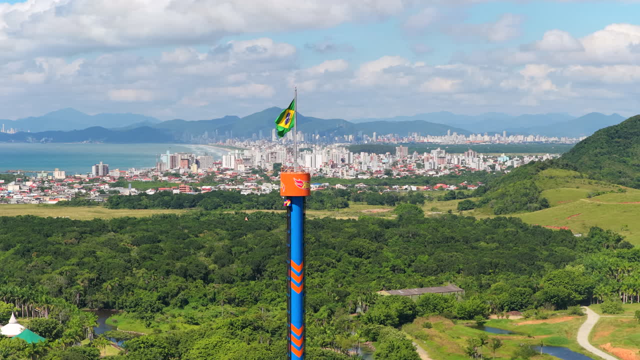 ブラジル南部の青空の下、ブラジル国旗を掲げた高層アミューズメントタワーと海岸線のスカイラインの空撮。
