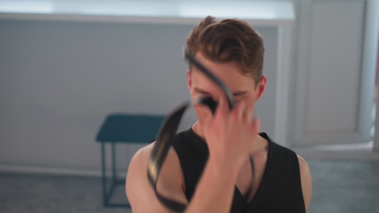 dancer ties belt around eyes before starting blindfolded choreography in spacious studio with stool backdrop and daylight streaming through windows showcasing dramatic movement