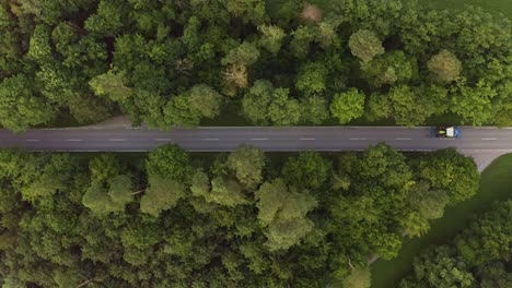A slow tractor is drining down a street from the right to the left, filmed with a drone directly from above - flying with the tractors direction - cars a passing by the agricultural vehicle