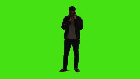 joven respondiendo a una llamada en el teléfono móvil de pie contra la pantalla verde con iluminación de bajo nivel 1