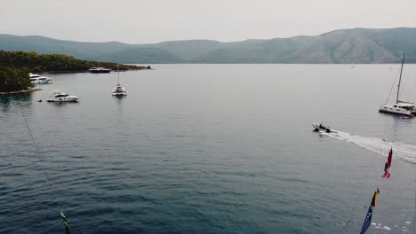 Drone-shot-of-a-yachts-cruise,-and-a-sailing-speed-boat-in-blue-sea-in-the-ocean,-island-background,-green-trees