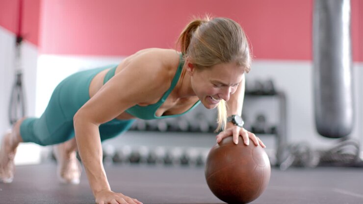 joven blanca en forma haciendo push up en la pelota de medicina en el gimnasio