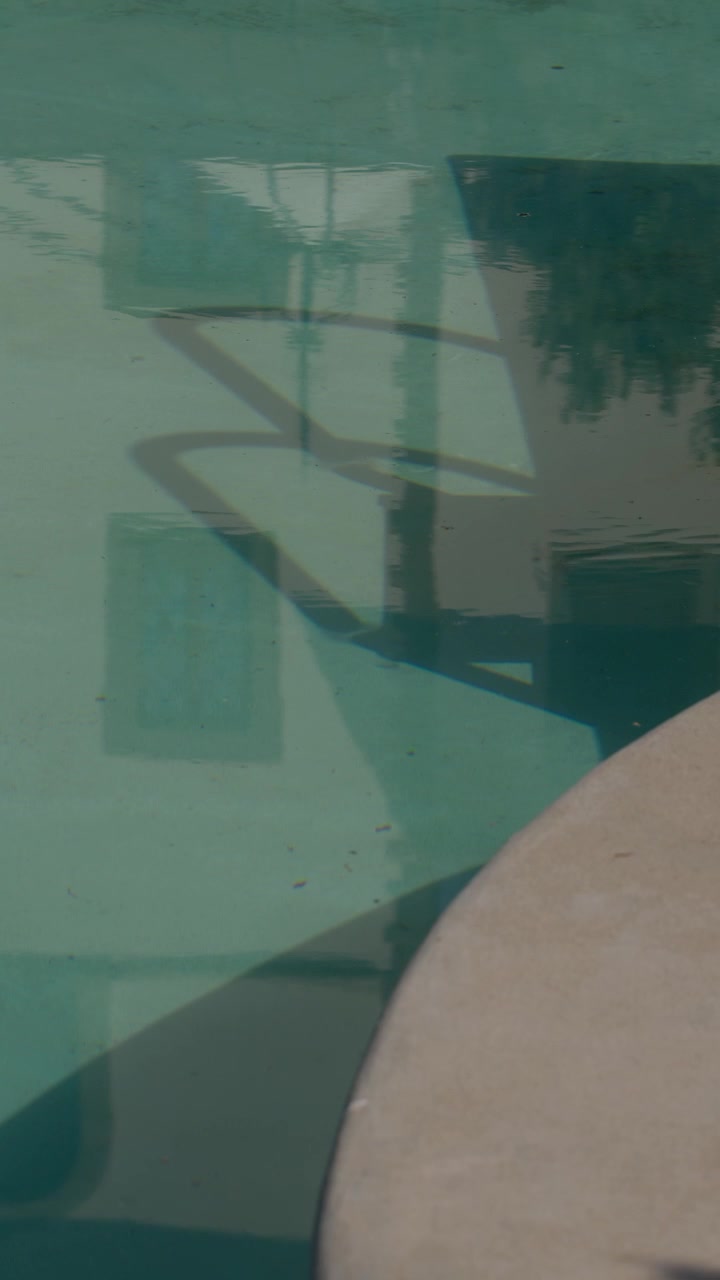 Reflection of villa windows and trees on calm pool water in outdoor daylight scene