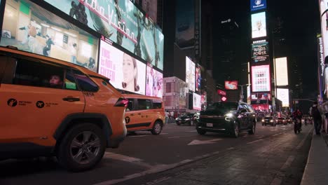 yellow taxi drives through times square at night with glowing billboards and city traffic around