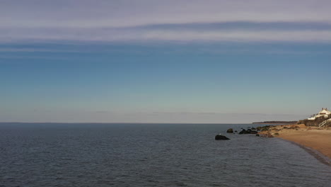 Ein-Niedriger-Blickwinkel-über-Das-Ruhige-Wasser-An-Einem-Leeren-Strand,-An-Einem-Tag-Mit-Blauem-Himmel