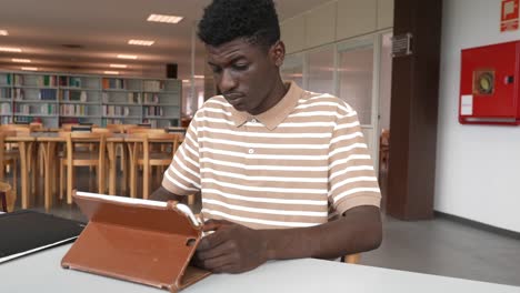 black student doing homework with tablet in library