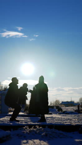 silhouette of a family of three outdoors in winter. man takes a baby and tosses him above the head. sun dazzles the shot. vertical video.