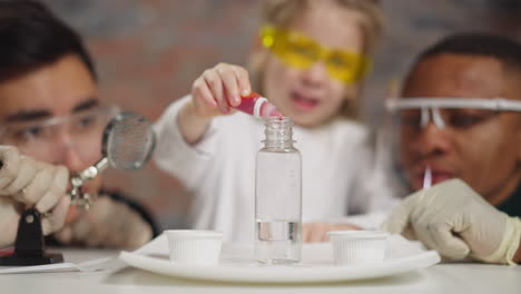 joyful girl drips red liquid into bottle with tutors in lab