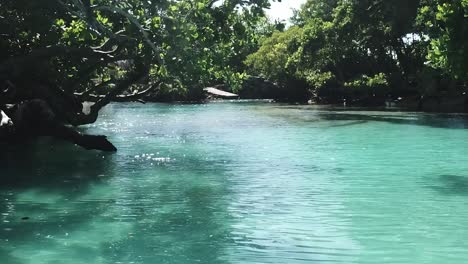 Drone-flying-low-on-blue-lagoon-Vanuatu-in-between-trees-water-glittering-in-sunshine