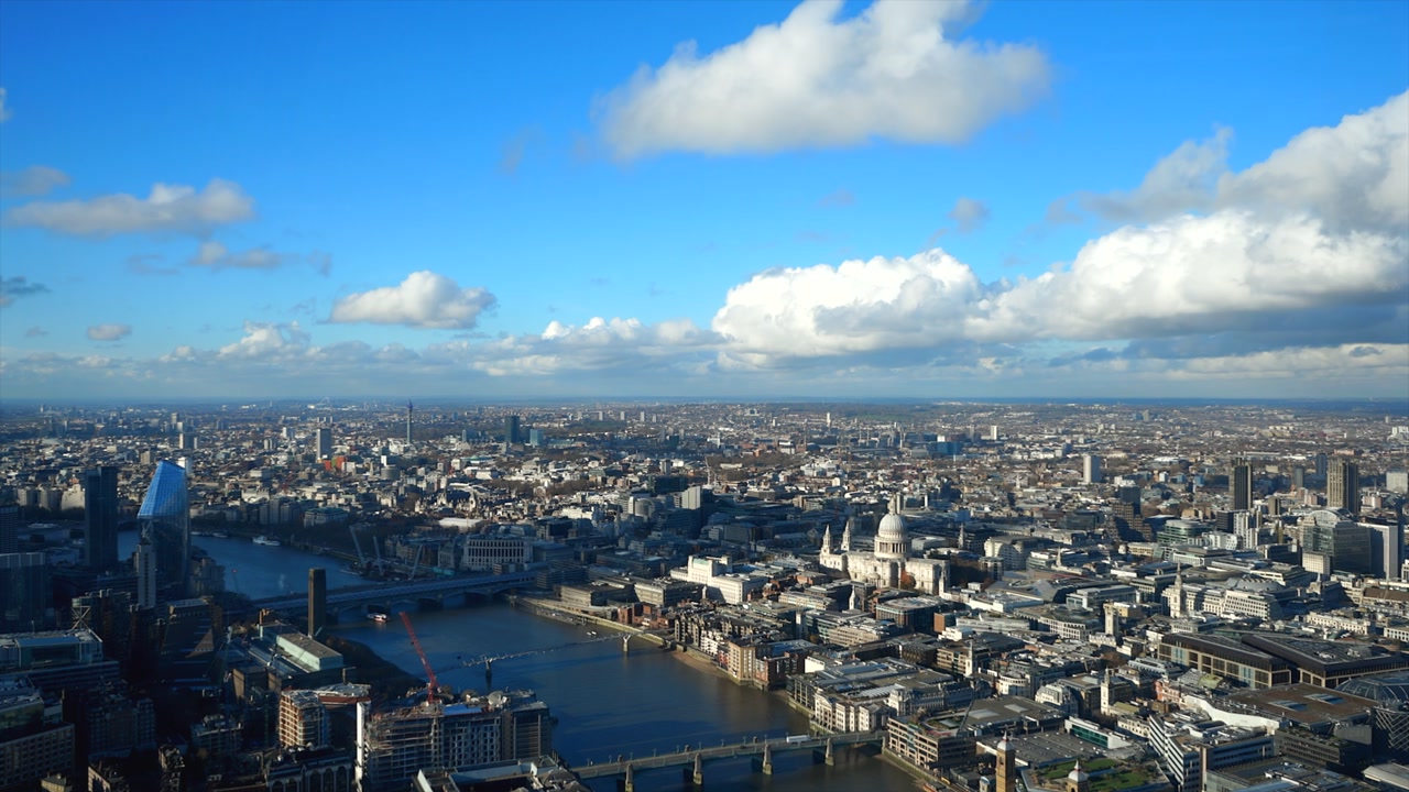 Stunning aerial footage captures London's iconic skyline, showcasing St Paul's Cathedral and the Thames. Brilliant blue skies illuminate the bustling urban landscape from above.