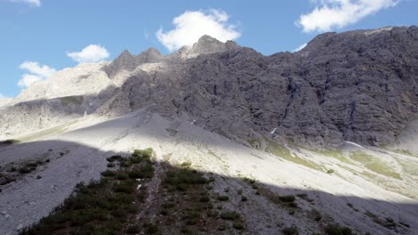 Aerial-drone-footage-reversing-slowly-to-reveal-a-the-summit-of-a-mountain-at-the-top-of-steep,-imposing-cliffs-in-Switzerland