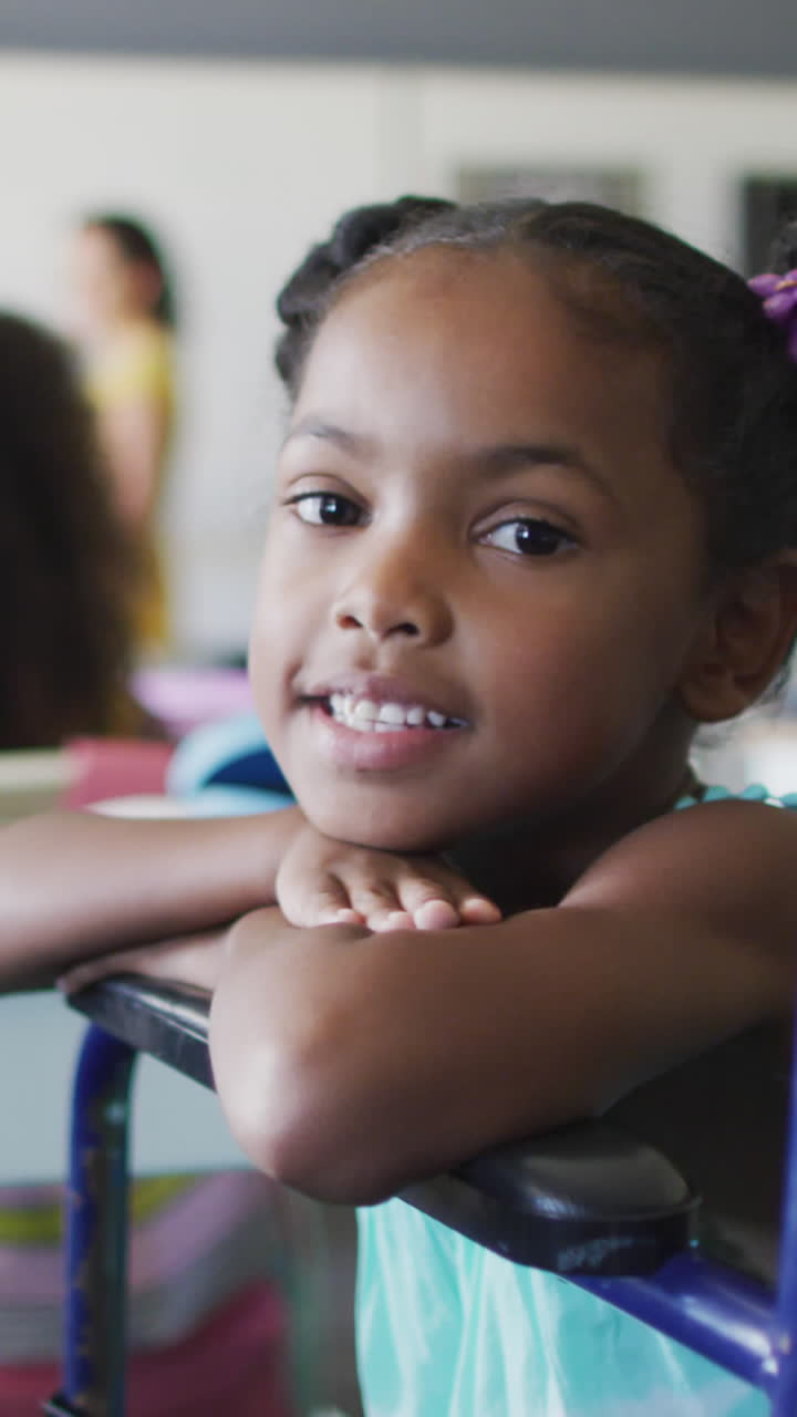 video de una feliz niña afroamericana discapacitada sentada en un escritorio en el aula