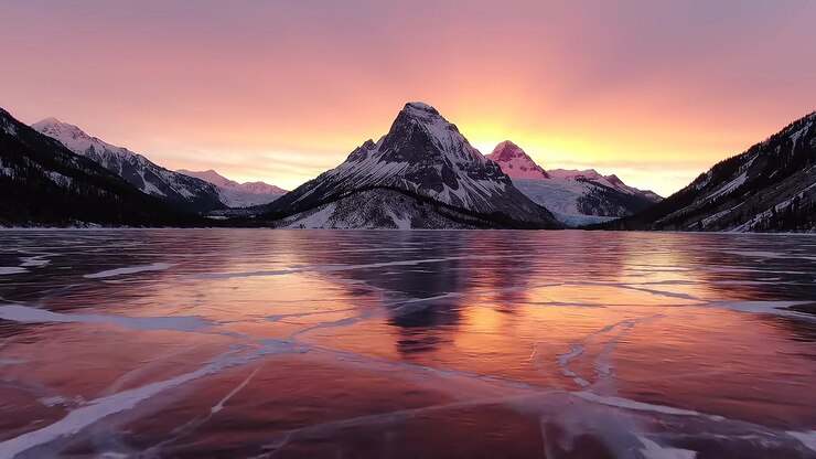 Riflesso del tramonto su un lago ghiacciato con montagne coperte di neve.