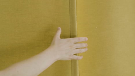 A-hand-reaches-out-to-an-ochre-colored-curtain-and-opens-it-in-slow-motion