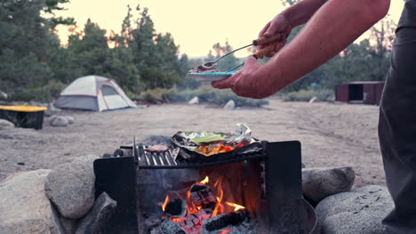 hombre asando bistec marinado y verduras en una fogata nocturna