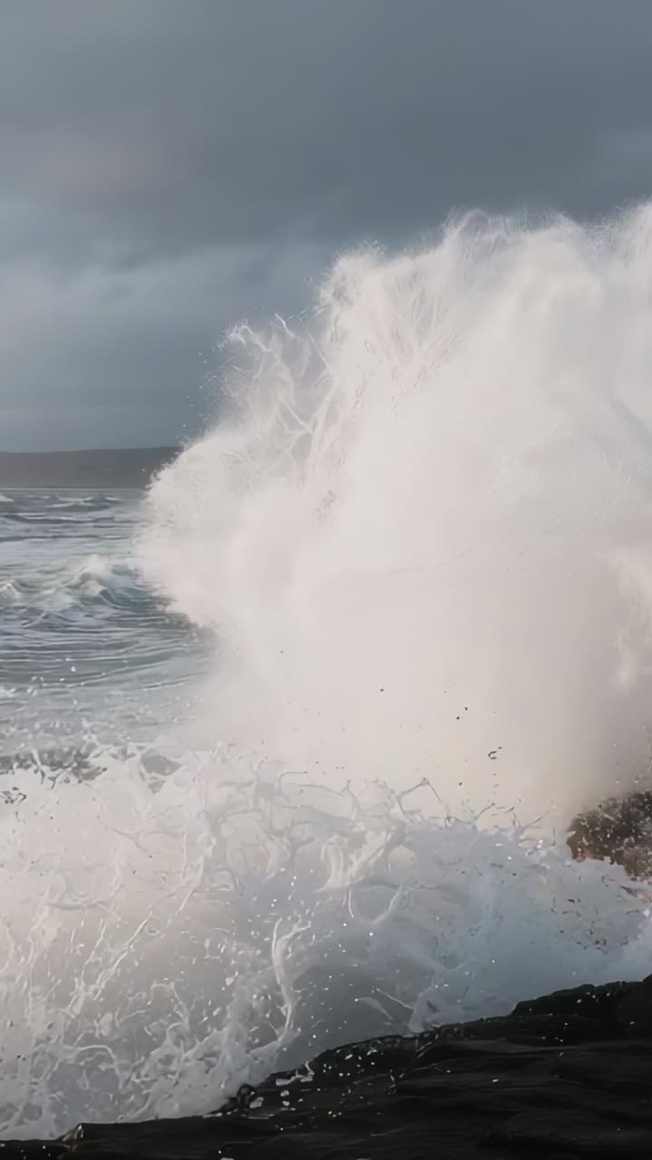 Vertical video: Crashing wave being pushed by swell, striking right cliff, forming plume and foam