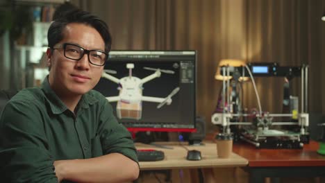 close up of asian engineer work on personal computer and 3d printer. he turns and warmly smiles into the camera